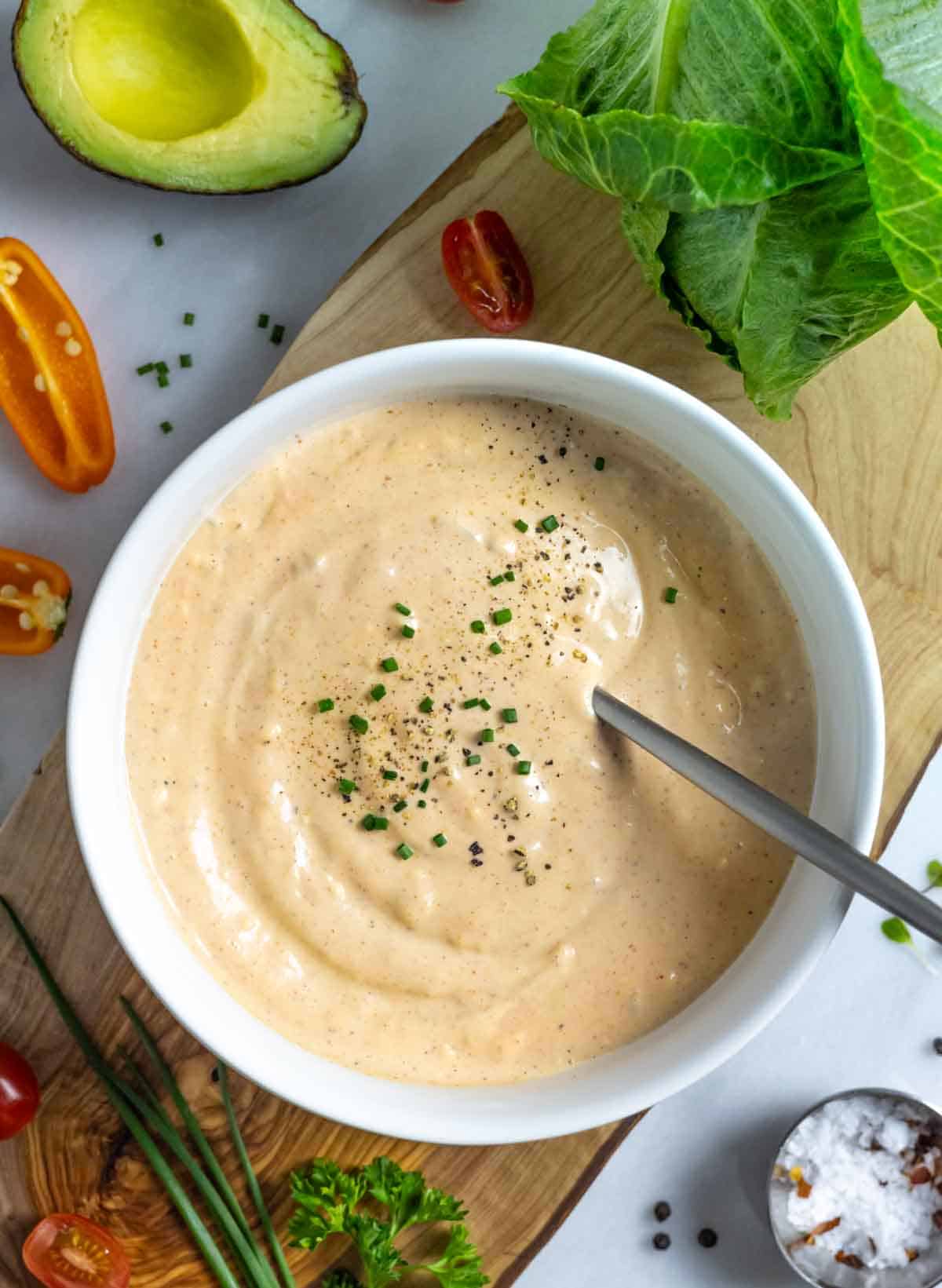 Dairy-free Thousand Island dressing in a white bowl with a spoon and topped with a sprinkle of fresh chives and black pepper.