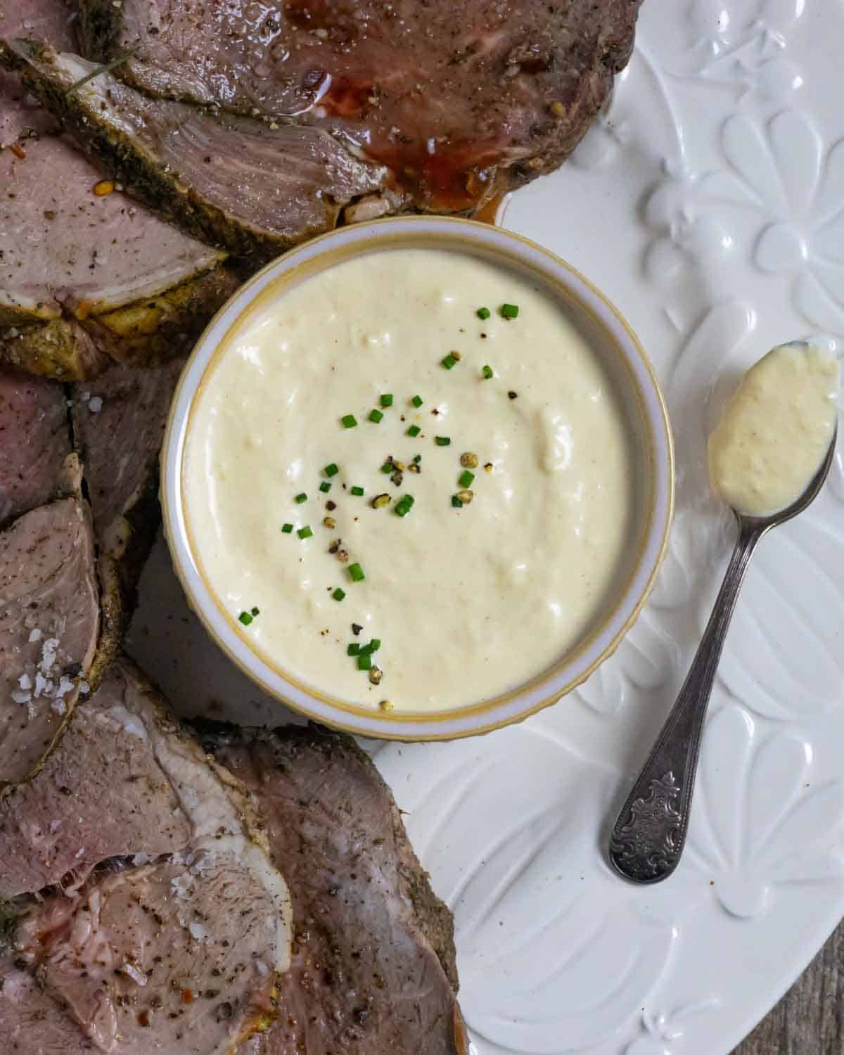 Ramekin of horseradish sauce on a white plate with slices of smoked lamb.