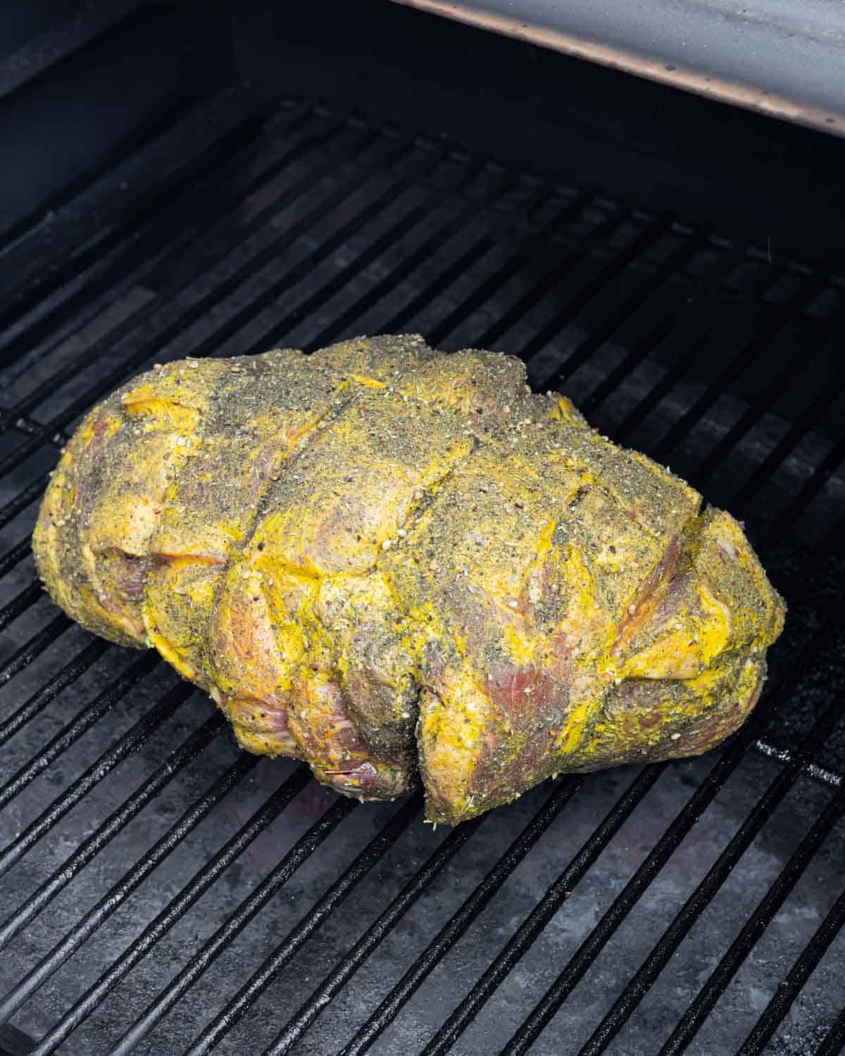 Lamb leg roast set onto smoker grill grates at start of smoking process.