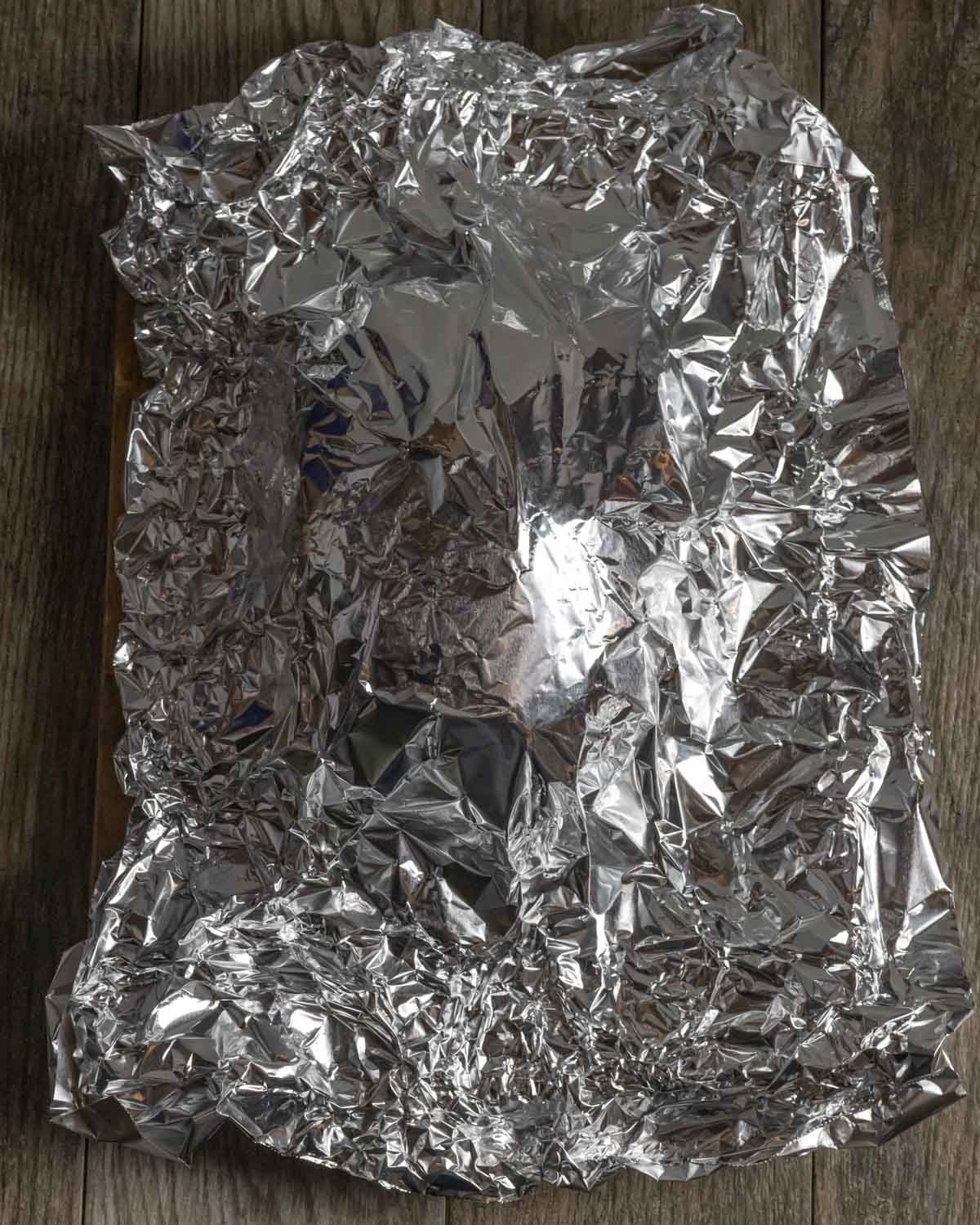 Lamb leg roast resting on a sheet pan covered with foil.