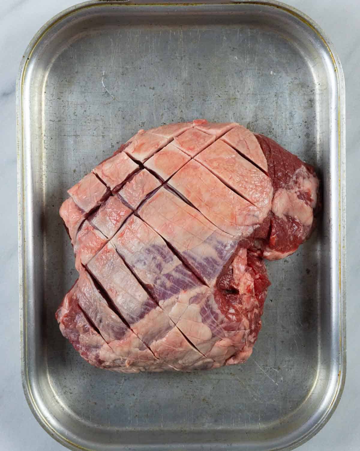 De-netted boneless lamb leg with cross-hatched scores cut into fat cap.