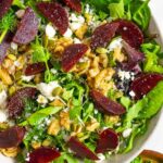 White bowl of beet and walnut salad topped with feta and nuts.