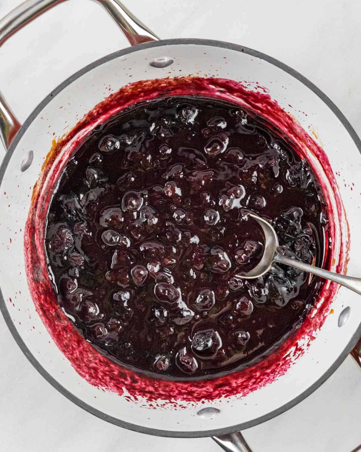 Cooked chunky blueberry bbq sauce in a pot with a spoon in it.