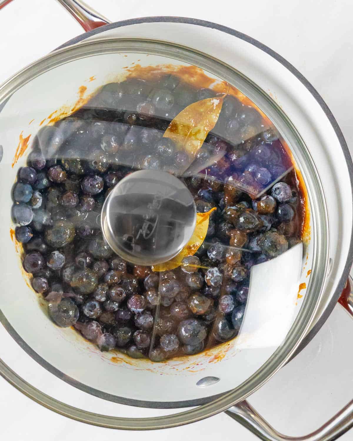 Blueberry bbq sauce ingredients simmering in a pot covered with a glass lid.