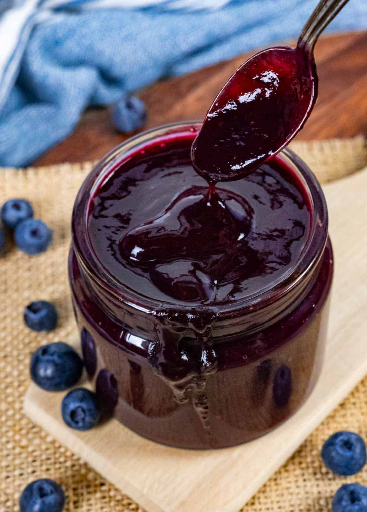 Glass jar of blueberry bbq sauce with a spoonful dripping into it.