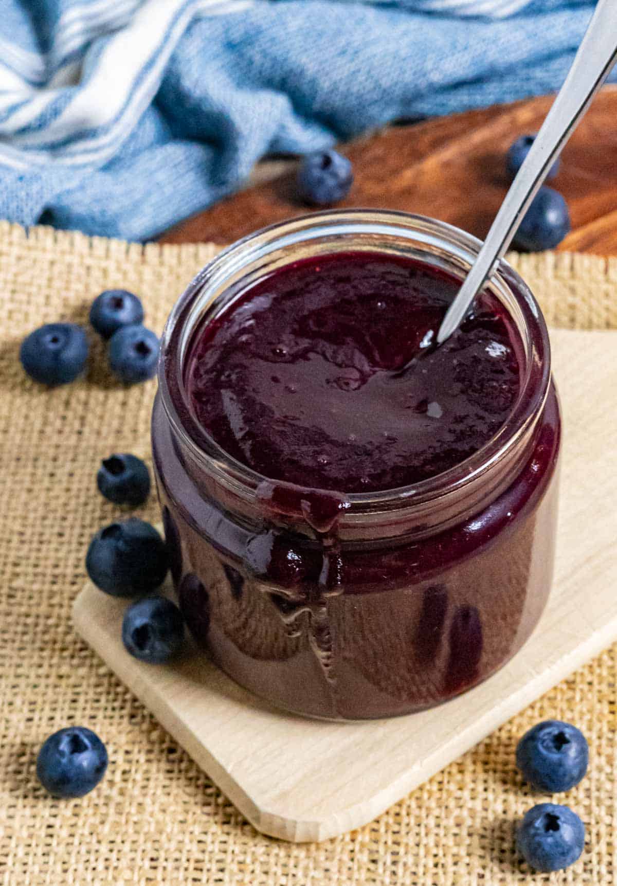 Blueberry bbq sauce in a jar with a spoon on a board with blueberries and a dribble of sauce.