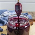 Jar of blueberry bbq sauce with spoon pouring sauce into the jar from above.
