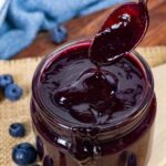 Blueberry barbecue sauce in a jar with a spoon pouring sauce into the jar.