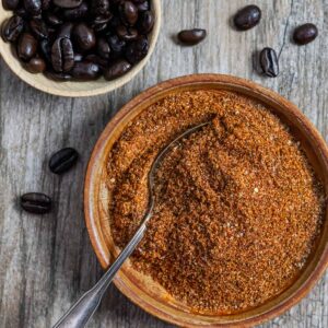 Bowl of coffee rub with spoon in it and another small bowl of coffee beans next to it.