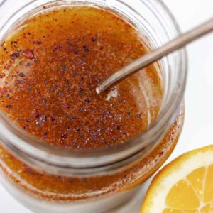 Sumac salad dressing in a small jar with a spoon and lemon wedge.