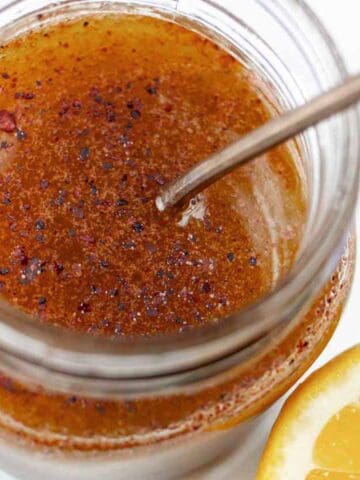 Sumac salad dressing in a small jar with a spoon and lemon wedge.