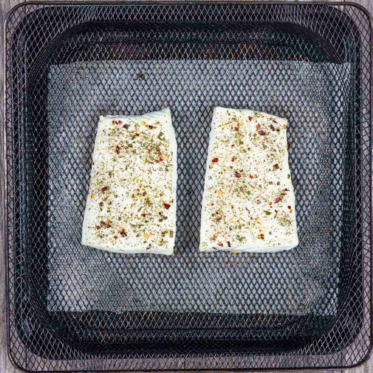 Halibut filets seasoned and fully cooked in air fryer basket.