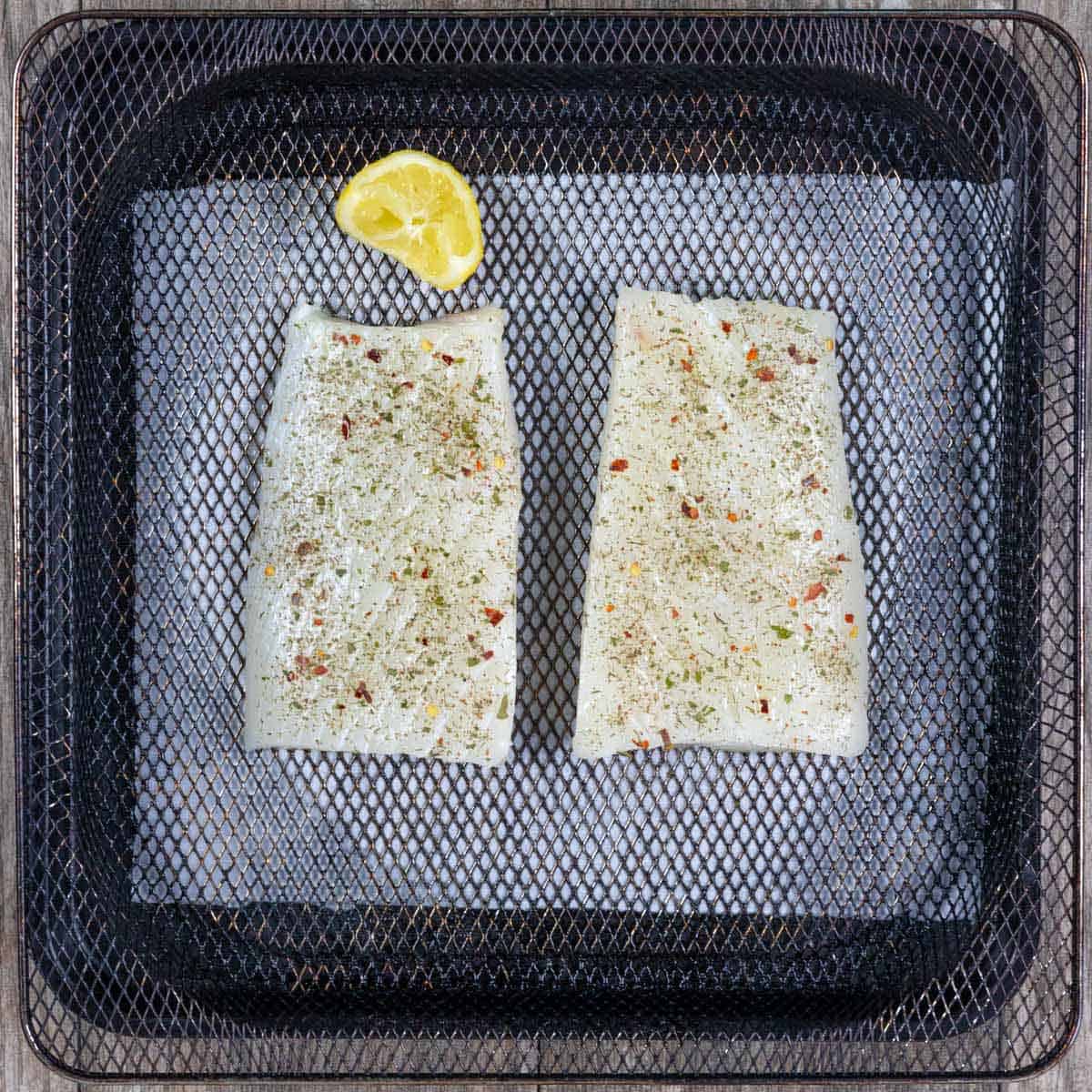 Two fish filets seasoned and on an air fryer basket ready to cook.