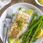 Air fried halibut sprinkled with herbs and citrus on a white plate with asparagus spears.