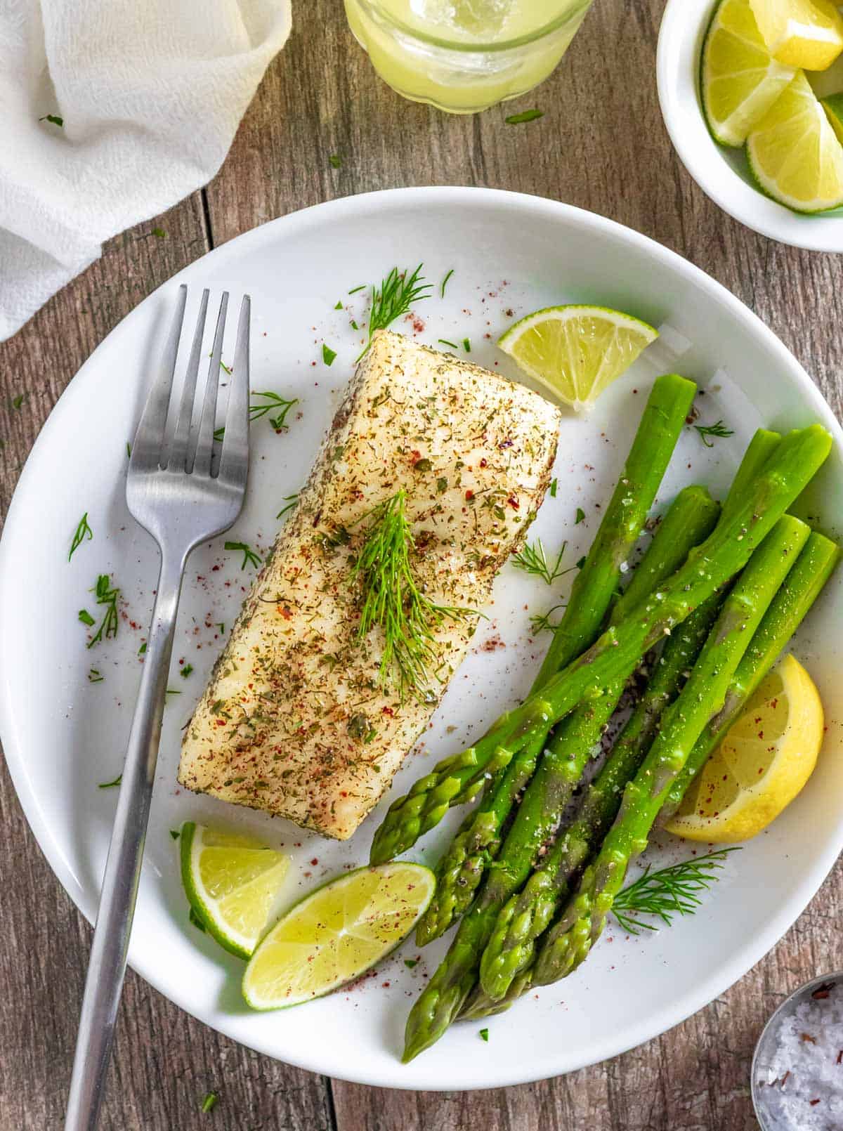 Air fried halibut sprinkled with herbs and citrus on a white plate with  asparagus spears.