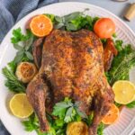 Whole convection oven roast chicken on a platter with herbs, citurs and garlic as garnish.