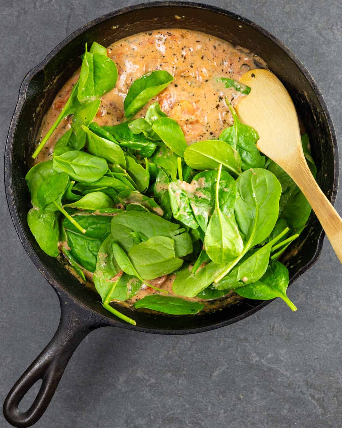 Simmered sauce with fresh spinach leaves added to a cast iron skillet.