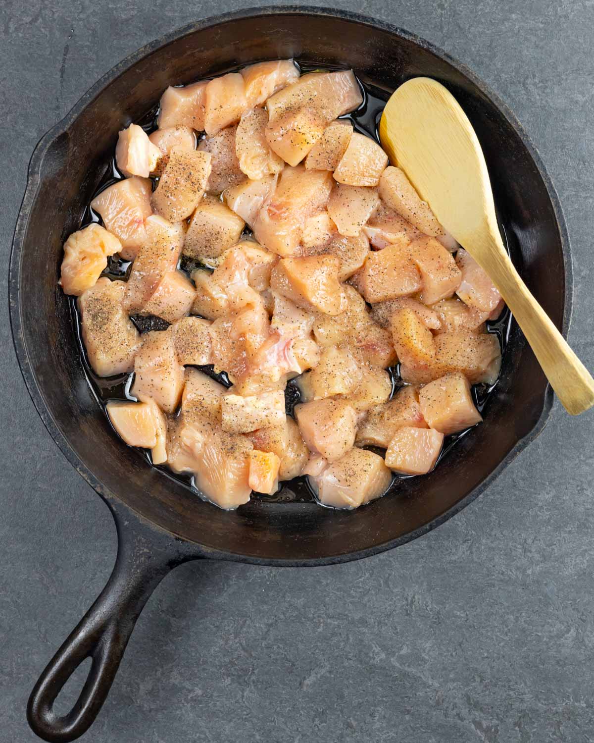 Diced chicken in a cast iron pan with a wood spoon ready to brown.