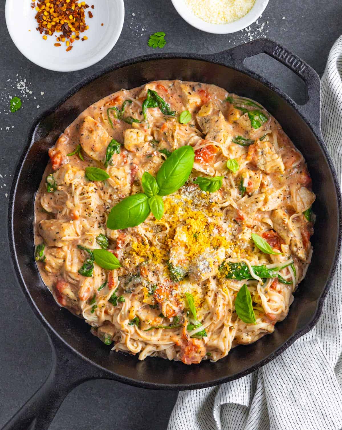 Marry me chicken pasta in a cast iron skillet topped with fresh basil leaves.