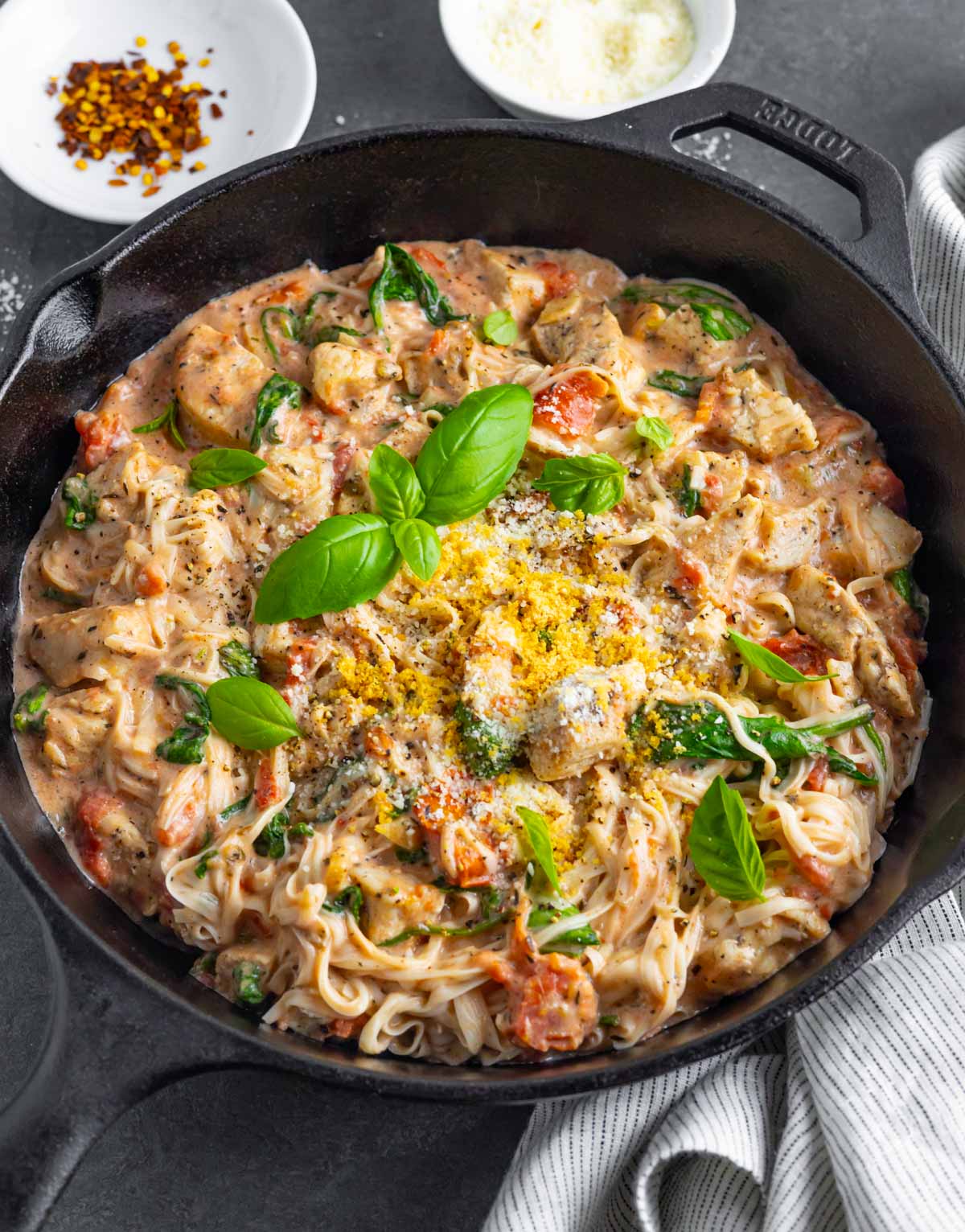 Skillet of marry me chicken with pasta topped with fresh basil on a grey board.
