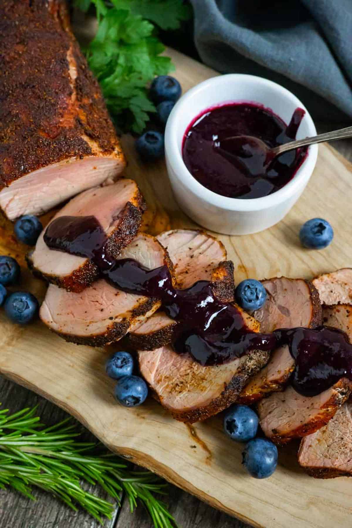 Slices of smoked pork tenderloin on a board with blueberry bbq sauce drizzled on them.