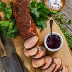 Smoked pork tenderloin sliced on a board with coffee rub and blueberry bbq sauce.