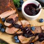 Slices of smoked pork tenderloin on a board with blueberry bbq sauce drizzled on them.