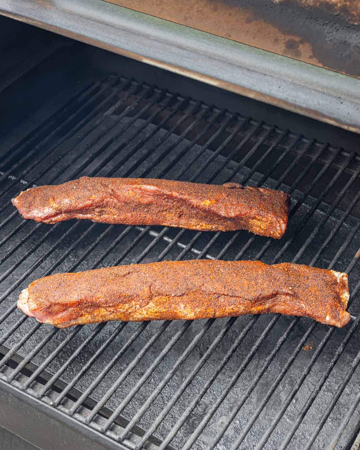 Pair of seasoned pork tenderloins placed on the smoker grill grates at the start of cooking.