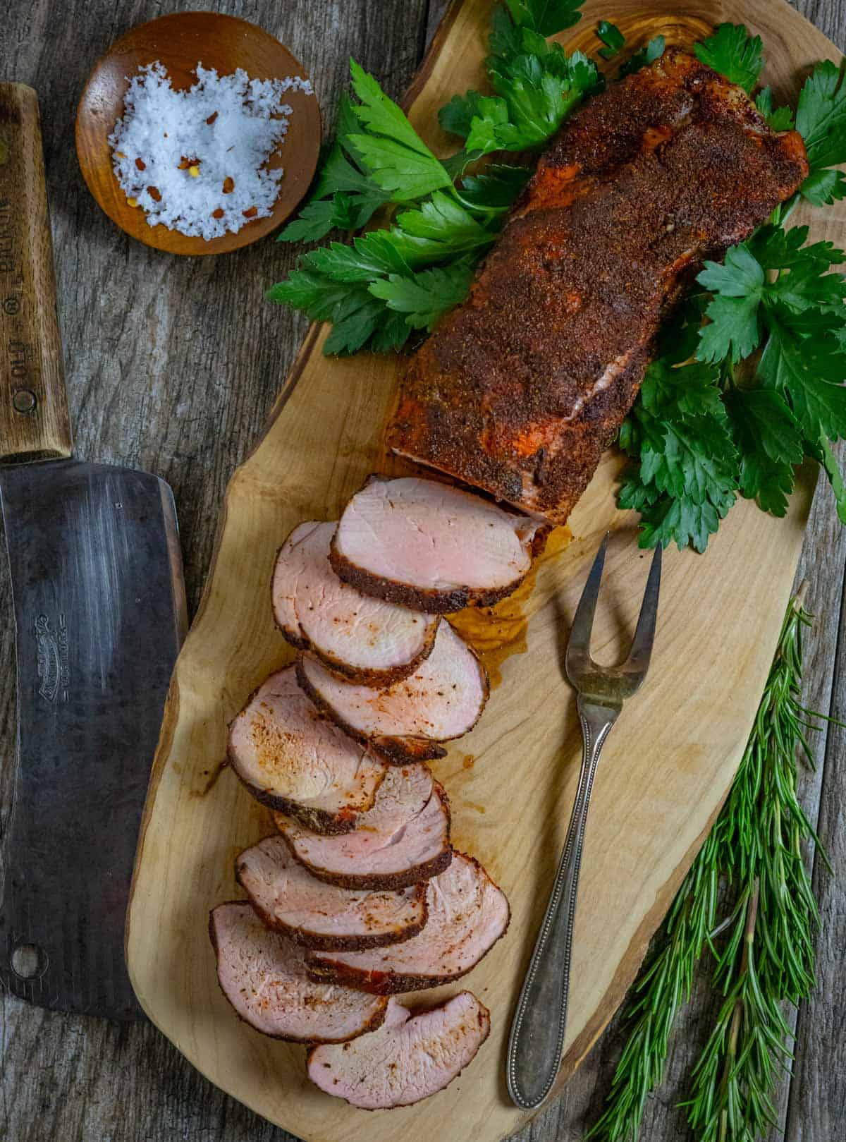 Pork tenderloin sliced halfway on a board with knife and carving fork.