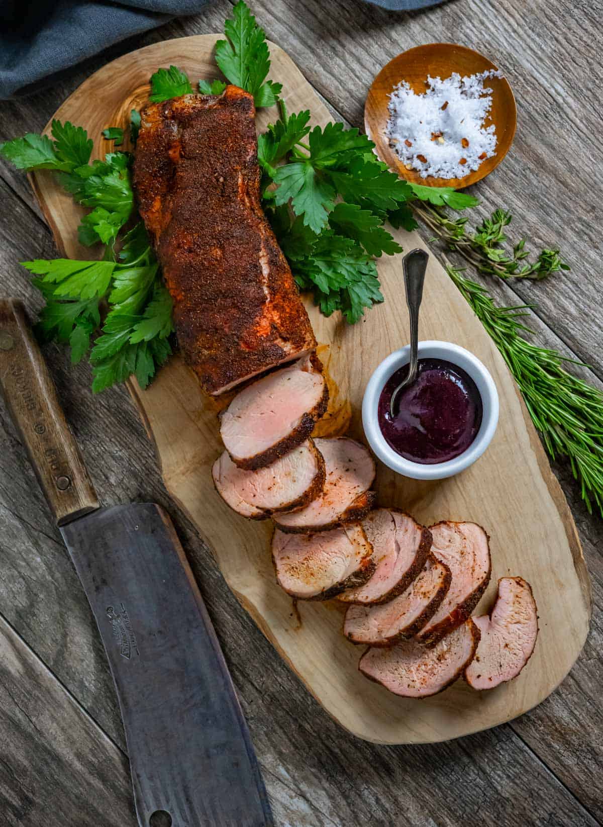 Smoked pork tenderloin with slices on a board with ramekin of blueberry bbq sauce.
