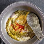 Homemade beef spice rub in a pewter bowl partially stirred with a fancy pewter measuring spoon.