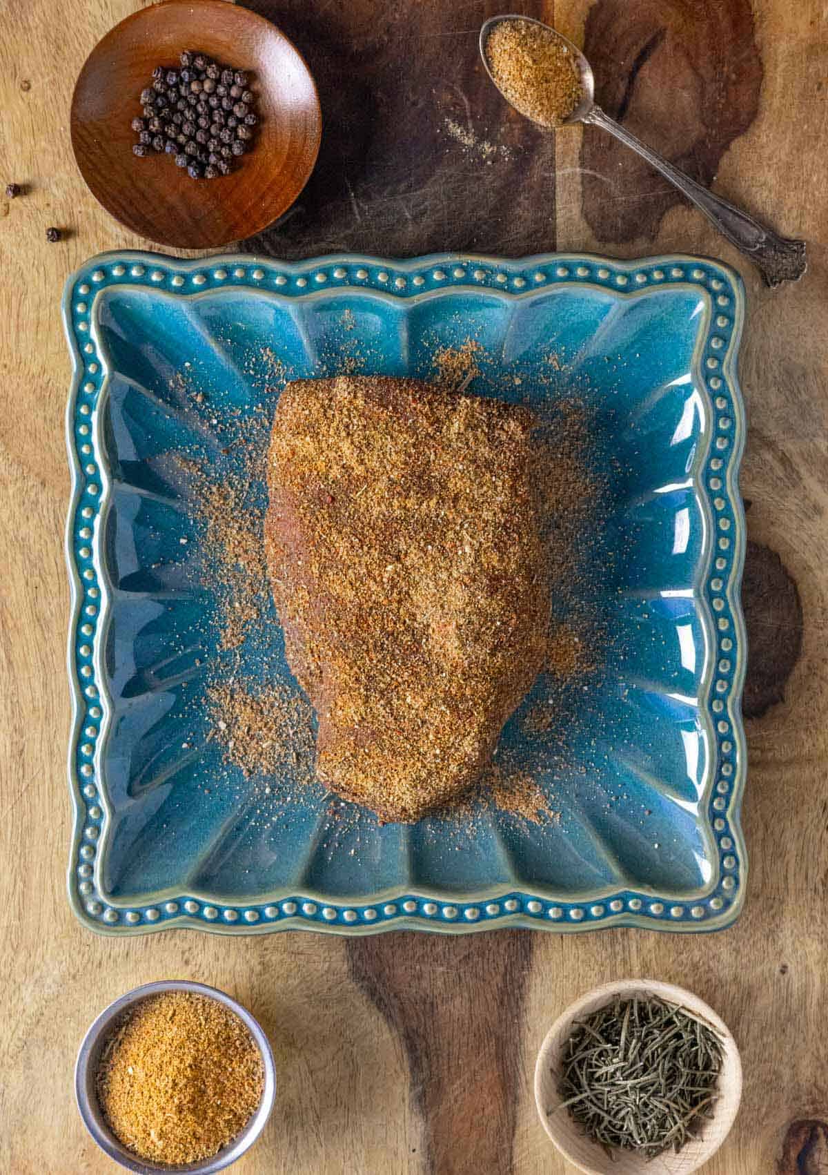 Beef sirloin steak covered in beef rub spices on a blue scalloped square plate.