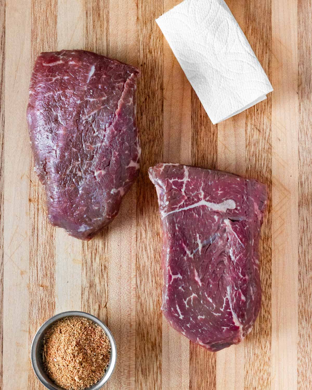 Two raw sirloin steaks on a board ready to pat dry and season.