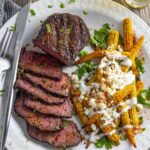 Sliced smoked sirloin on a white plate with a baby corn salad.