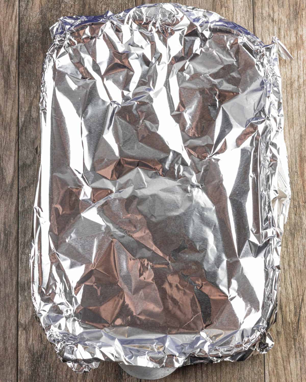 Pan covered in foil containing two smoked sirloin steaks, resting.