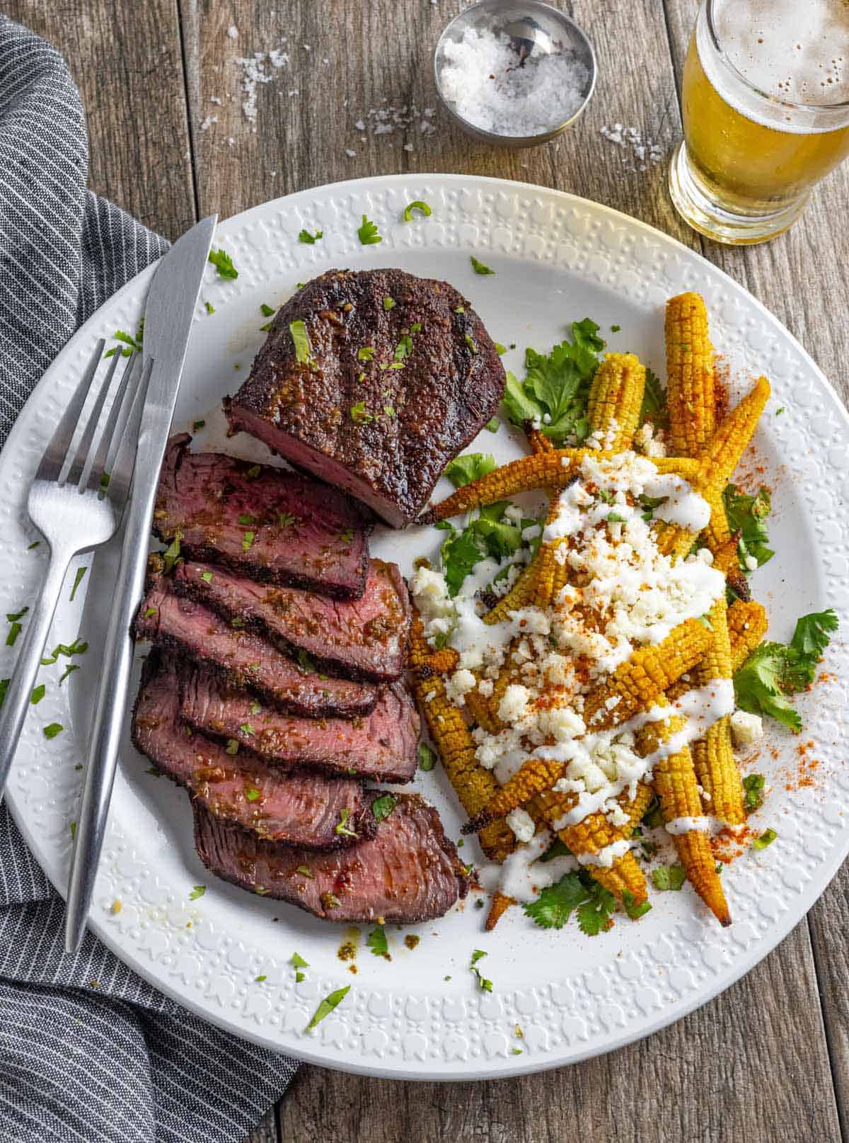 Sliced smoked sirloin on a white plate with a baby corn salad.