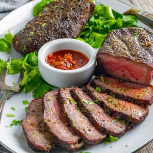 Sliced smoked sirloin steak on a plate with chimichurri sauce and a garnish of cilantro.