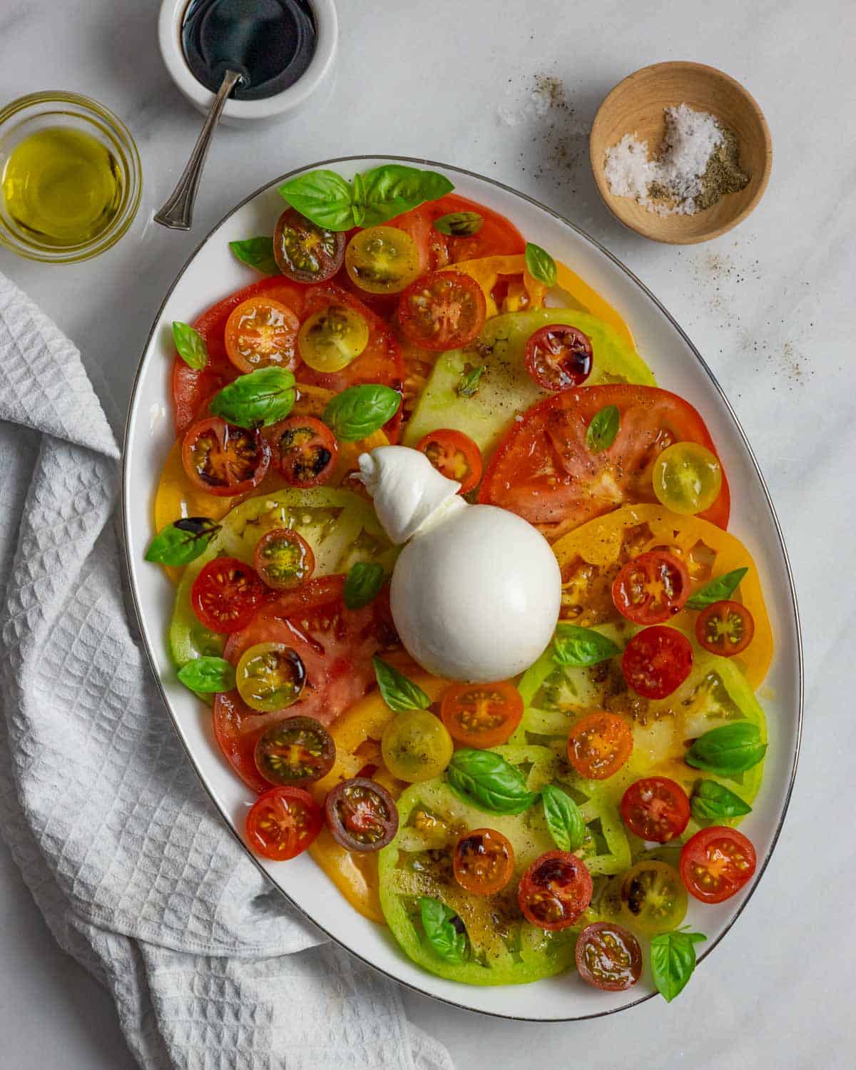 Caprese salad ready to serve with ball of burrata cheese placed in the center of the platter.