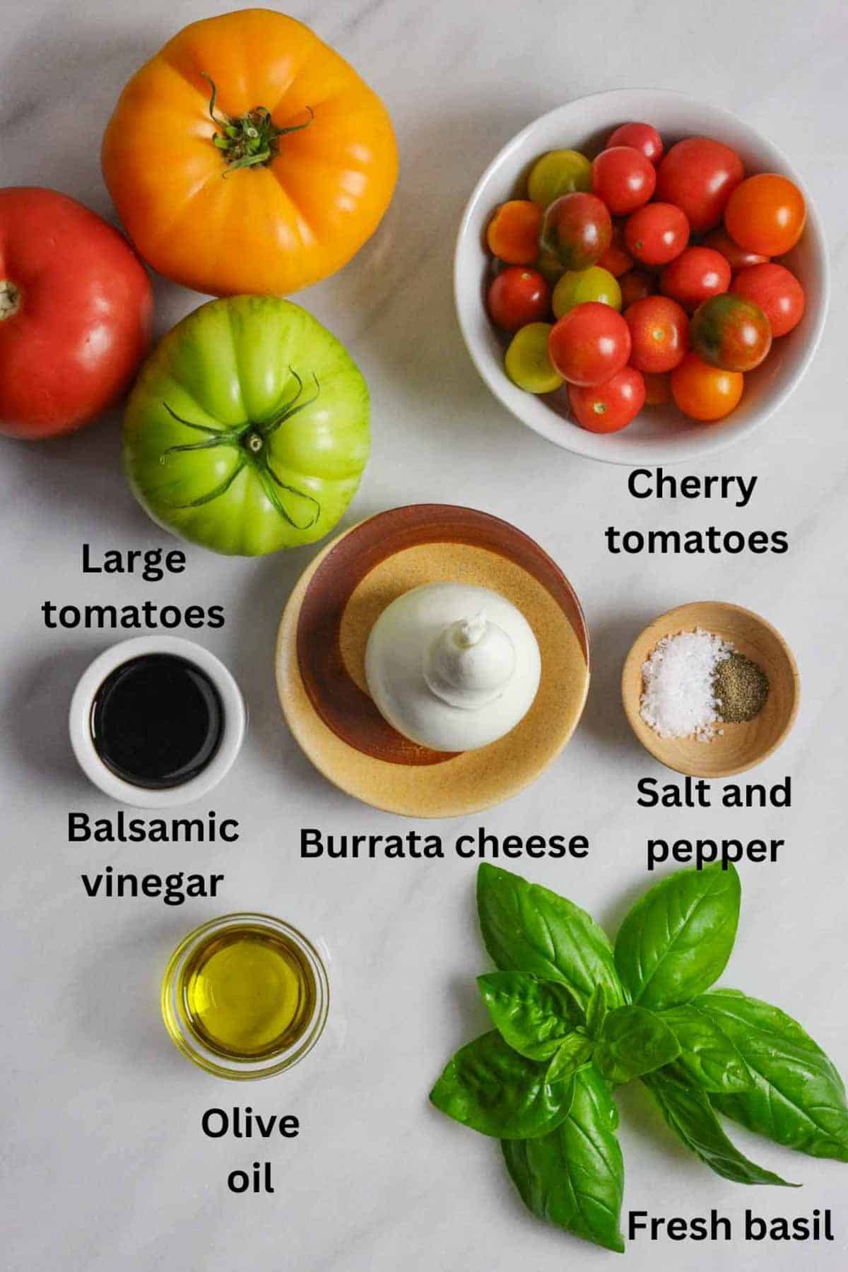 Ingredients for burrata caprese salad on a marble board with black text labels.