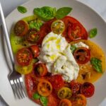 Burrata caprese served on a plate with a fork topped with fresh basil leaves.