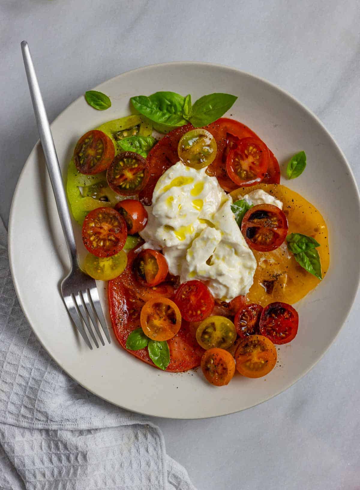 Burrata caprese served on a plate with a fork topped with fresh basil leaves.
