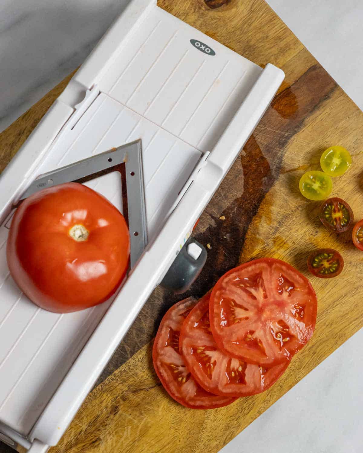 Red tomato on a mandolin slicer on a board with additional slices.