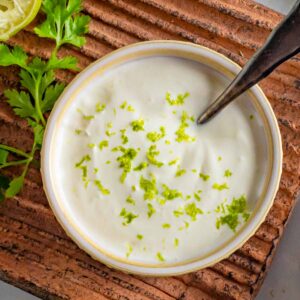 Bowl of lime crema with lime zest on top sitting on a clay tray.