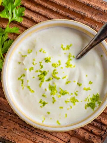 Bowl of lime crema with lime zest on top sitting on a clay tray.