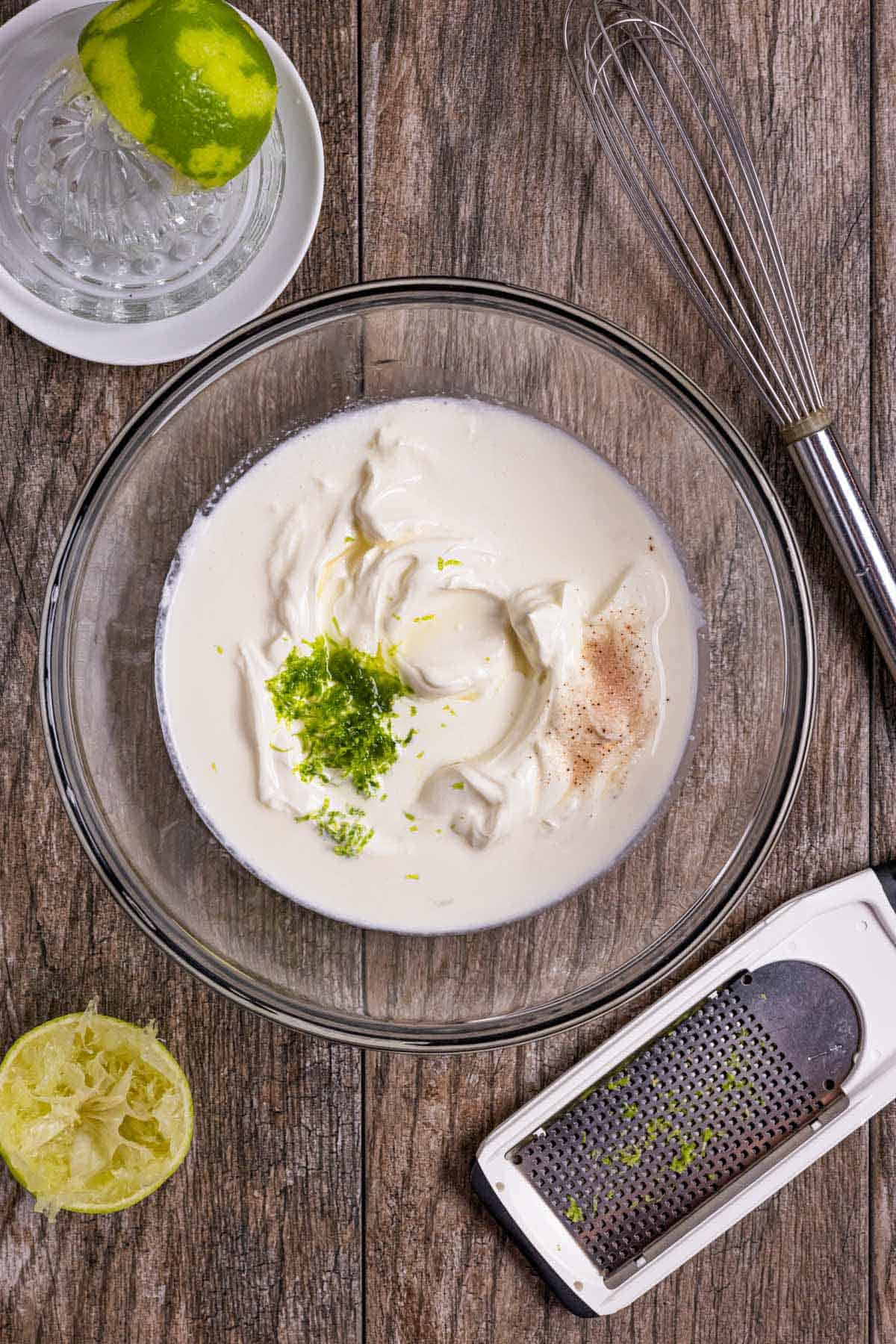 Glass bowl of unmixed crema ingredients with a whisk and lime zest on the side.