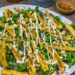 White plate of baby corn microgreens salad topped with cotija cheese and crema dressing.