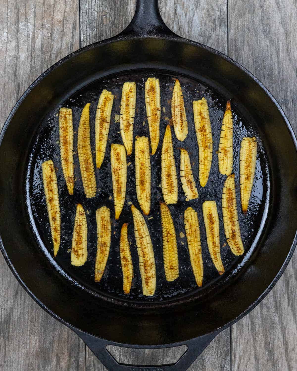 Cast iron pan with seasoned baby corn halves ready to brown.