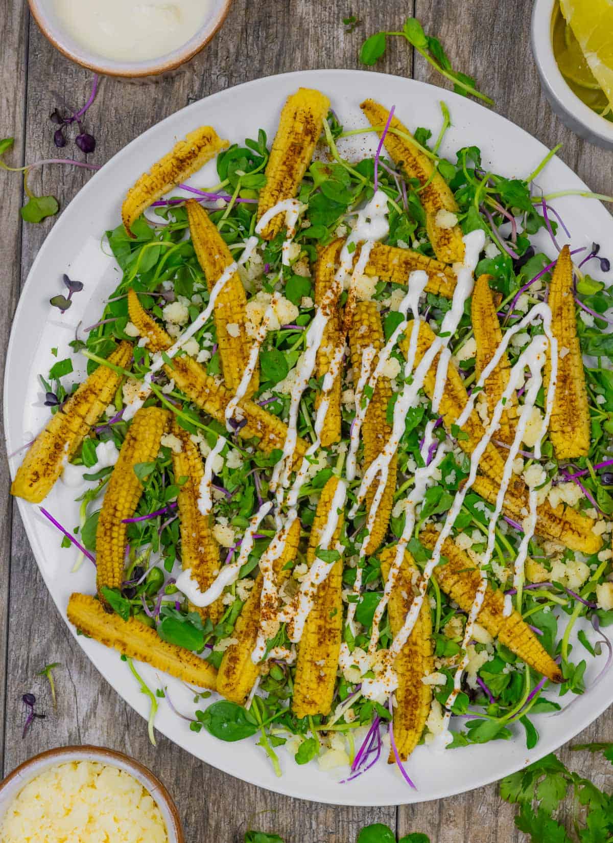 Microgreens salad on a white plate with  roasted baby corn and topped with crema dressing.