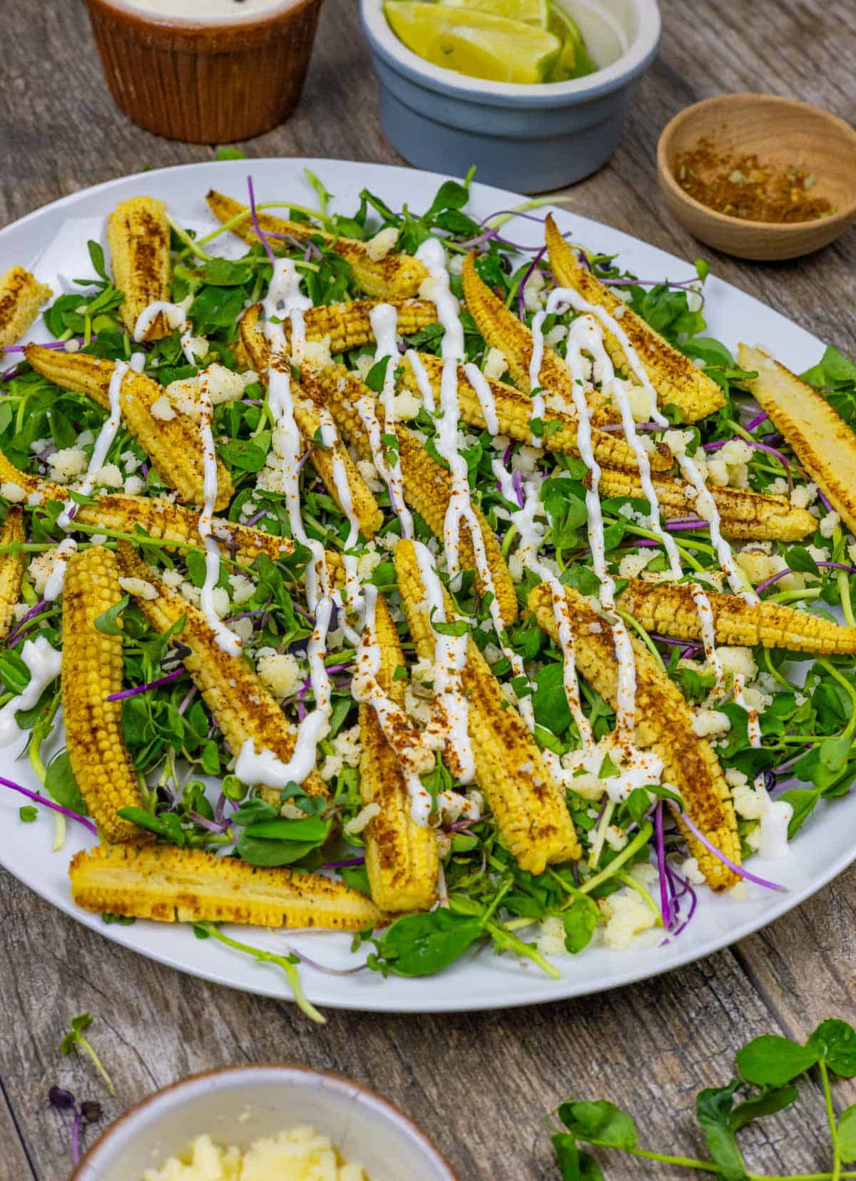 White plate of baby corn microgreens salad topped with cotija cheese and crema dressing.