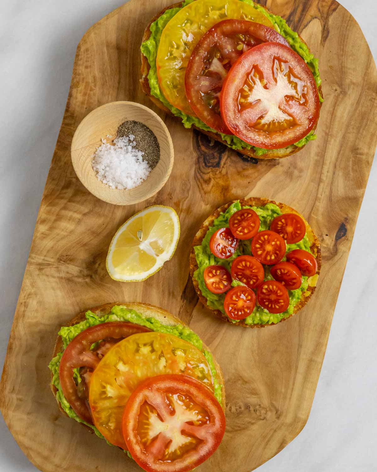 Three slices of low-fodmap avocado toast with a lemon wedge and bowl of salt and pepper.